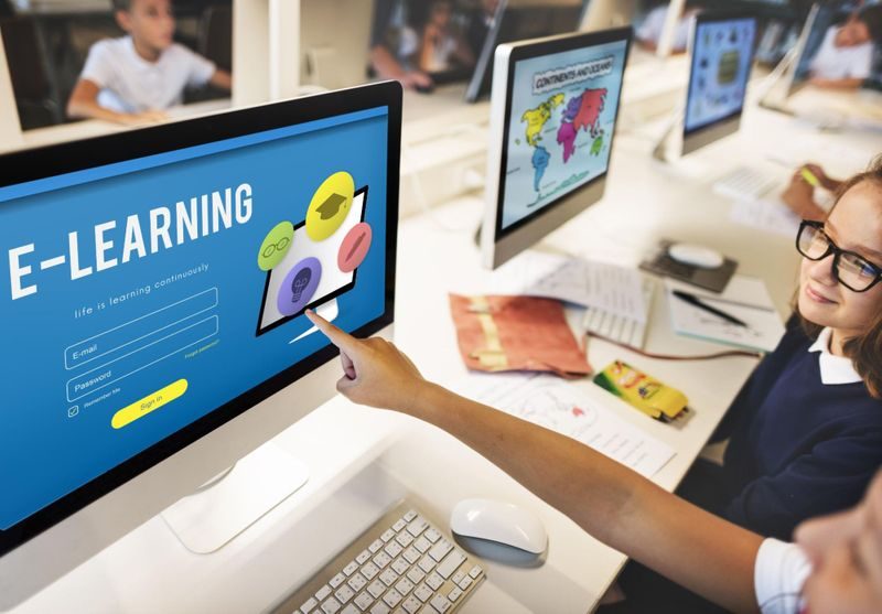 Students in modern classroom pointing at monitor displaying E-Learning course