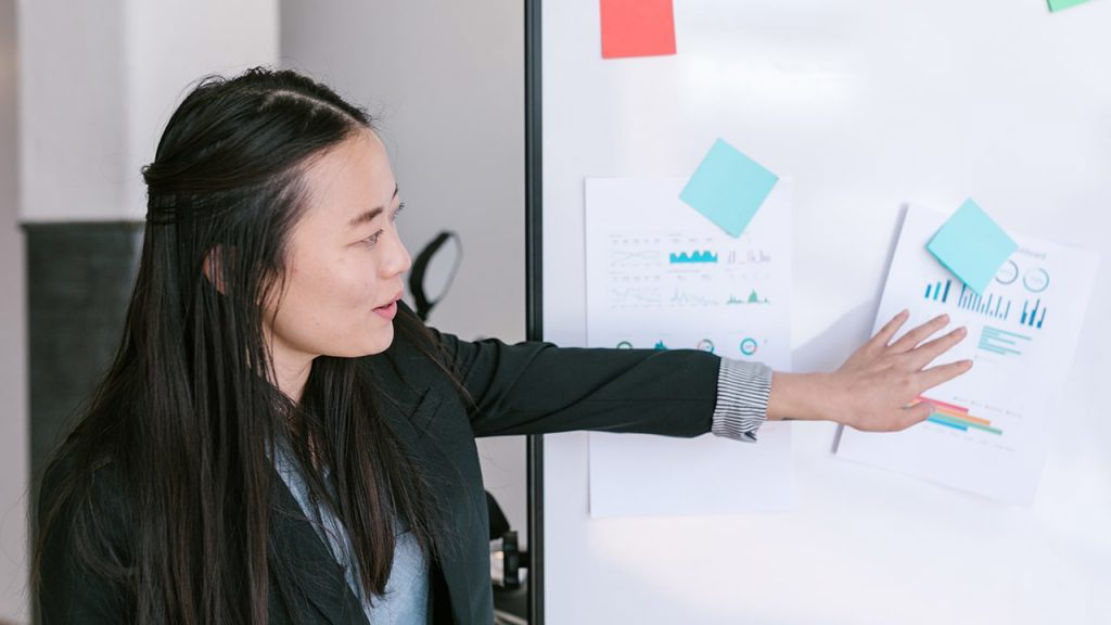 Asian woman pointing at a document magnetized to a whiteboard