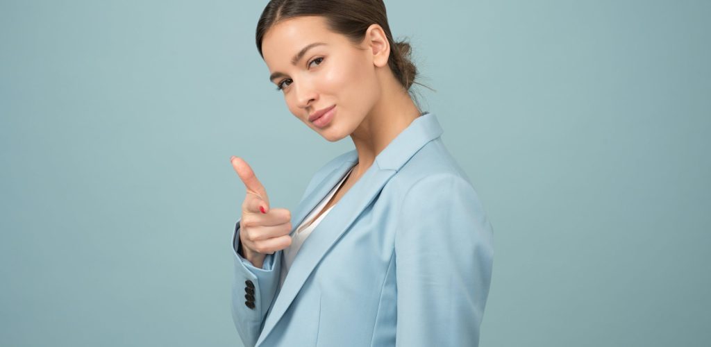 A woman in a blue suit pointing at the camera