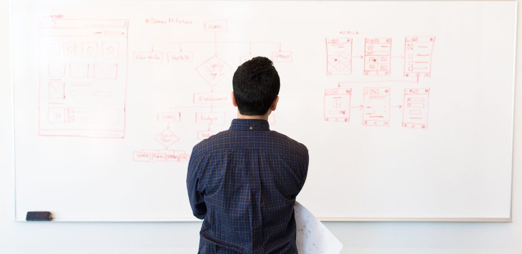 Man stood in front of a white board with plans on it